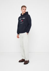 Felpa navy con logo frontale e design della bandiera francese; presenta una grande tasca a marsupio. Abbinate a pantaloni chiari e scarpe marroni.