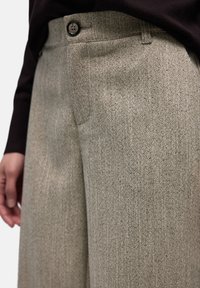 Weit geschnittene Heringbone-Hosen in Beige und Grau mit Knopfverschluss, Seitentaschen und strukturiertem, gewebtem Stoff.