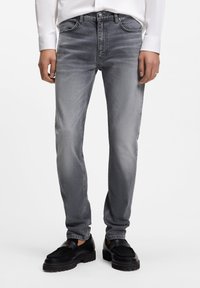 Jeans de mezclilla gris ajustados con acabado descolorido, diseño de cinco bolsillos y costuras en contraste, combinados con zapatos negros sin cordones.