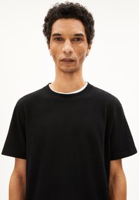 T-shirt en coton noir avec un col rond, des manches courtes et une coupe décontractée. Présente une texture subtile et ne comporte aucun motif ni logo visible.