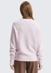Pulover roz deschis, cu textură moale, cu un croi lejer, mâneci lungi și manșete cu nervuri, asociat cu pantaloni maro.