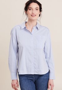Camicia button-up a righe blu chiaro con colletto, taschino sul petto, maniche lunghe e vestibilità comoda. Indossata con jeans blu scuro.