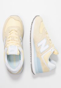 Gule sneakers i ruskind og mesh med lyseblå detaljer og hvid "N"-logo. Har en polstret krave og en struktureret gummiydersål.