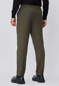 Joggers vert olive avec une taille à cordon, une poche latérale et des jambes effilées. Fabriqués dans un matériau doux et lisse, assortis à des chaussures noires.