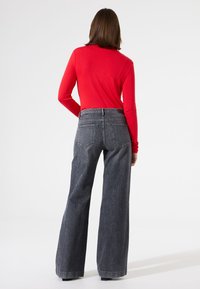 Rode langslavende top met een gestructureerde afwerking, gecombineerd met wijdvallende donkergrijze jeans met achterzakken en een hoge taille.