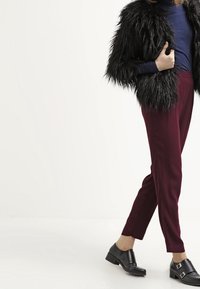 Černá umělá kožešinová bunda, námořnický rolák, burgundské kalhoty na míru a černé boty s přezkami, které předvádějí různé textury a barvy.