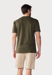 Olive green, short-sleeve t-shirt made of soft fabric, paired with light beige shorts, viewed from the back. Simple design, relaxed fit.