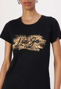 T-shirt nera in cotone con un design a stampa leopardata e il testo "Liu Jo" in corsivo su una pennellata orizzontale di colore marrone chiaro. Maniche corte.