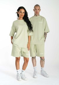 Conjunto deportivo de algodón verde claro que incluye camisetas oversized y pantalones cortos, con detalle de cordón y logo "MULTIPLY" en blanco.