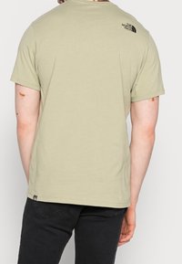 Olivgrön kortärmad t-shirt med rund hals och en liten svart logotyp på den övre ryggen. Blandat bomullsmaterial, avslappnad passform.