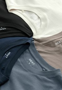 Vijf T-shirts in verschillende kleuren: zwart, gebroken wit, lichtgrijs, donkerblauwgroen en bruin, met ronde halslijnen en "NEXT" labels.