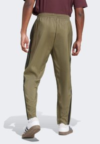 Pantalones deportivos de color verde oliva con un ajuste relajado, que cuentan con rayas laterales negras, una cintura elástica y una textura suave y brillante.