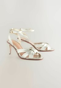 Metallisch zilveren hoge hakken sandalen met een bandjesontwerp, voorzien van een geknoopte detail aan de voorkant en een verstelbare enkelband.