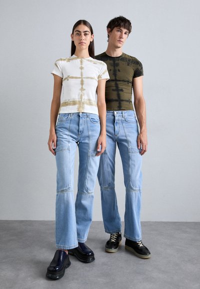 To modeller har på seg uformelle antrekk: en hvit og beige tie-dye t-skjorte sammen med lyseblå vide jeans, og en mørkegrønn tie-dye t-skjorte med lignende jeans.