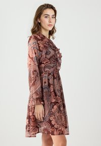 Langärmliges Paisleykleid in Brauntönen und Orange mit gerüschtem Ausschnitt, fließender Silhouette und strukturiertem Stoff.