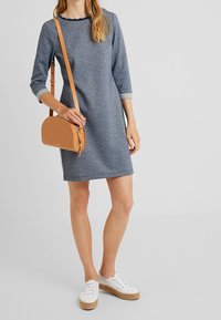 Grå långärmad klänning med en scalloped krage, kombinerad med en ljusbrun crossbody-väska och vita platåskor. Slät tygstruktur.