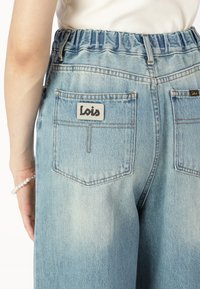 Pantaloni din denim albastru deschis cu talie elastică, având două buzunare la spate cu detalii cusute și un patch cu logo-ul "Lois".