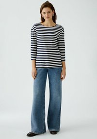 Gestreiftes Oberteil mit marineblauen und weißen horizontalen Streifen, Bootsausschnitt und Dreiviertelärmeln, kombiniert mit weit geschnittenen blauen Jeans.