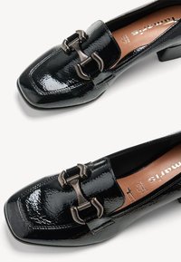 Mocassins en cuir verni noir avec détail mors métallique et petit talon carré, avec bout carré et doublure intérieure en cuir marron clair.