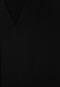 Záber zblízka na čiernu látku so švom v tvare V a jemným textúrovaným šitím.