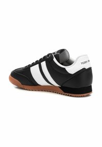 Baskets noir et blanc avec une tige en cuir lisse, trois bandes blanches, semelle en caoutchouc et un accent de talon noir texturé.