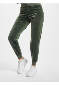 Gröna velourjoggers med ribbade muddar, som har en slät textur och sidopaneldesign, kombinerade med vita sneakers.