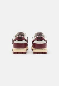 Nike sneakers with a white upper, maroon accents, rubber sole, and textured leather. Features logo on heel and a contrasting midsole.