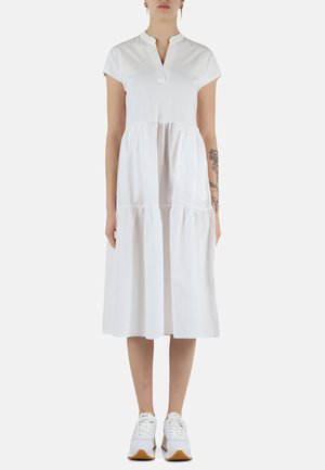 Abito bianco in cotone con colletto corto, maniche corte e gonne a strati. Indossato con sneakers bianche, evidenziando uno stile informale.