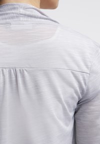 Jasnoszara bluzka z teksturowanego dzianiny, z okrągłym dekoltem i marszczonym szwem z tyłu, wyróżniająca się miękkim i przewiewnym materiałem.