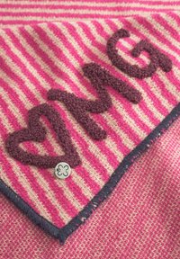 Gebreide stof in roze en crèmekleurige strepen heeft donkercognackleurige, gestructureerde letters "OMG" en een hart, met een kleine decoratieve knop.