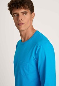 Blauwe T-shirt met lange mouwen, gemaakt van zachte stof, heeft een ronde halslijn en een enkele borstzak met een gladde textuur.