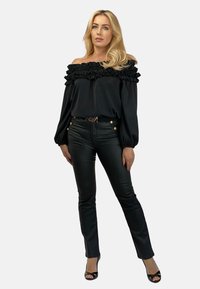 Czarna bluzka bez ramiączek z falbaniastym dekoltem, zestawiona z czarnymi, skórzanymi spodniami o wysokim stanie z złotymi guzikami.