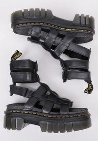 Sandalias gladiador de cuero negro con suelas gruesas y resistentes y costuras amarillas, que cuentan con múltiples correas ajustables y tiradores.