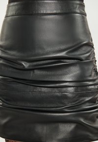Falda de cuero negro con textura arrugada y acabado suave. Cuenta con una cinturilla ancha y un ligero brillo, resaltando la calidad del material.