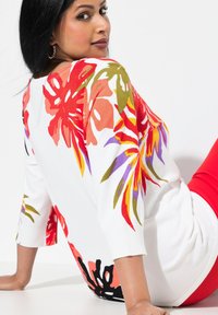 Maglione lavorato a maglia con design floreale colorato in rosso, rosa, viola e verde su uno sfondo bianco. Presenta maniche a tre quarti e orlo a coste.
