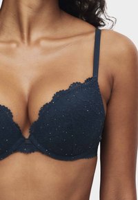 Marineblauwe kanten beha met geschulpte randen, bloemmotief en kleine fonkelende accenten. Verstelbare bandjes, gevormde cups en een gladde textuur.