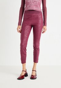 Leggings bordeaux ajustés avec un motif léopard subtil, associés à un haut à manches longues cropped dans une teinte plus claire de bordeaux.