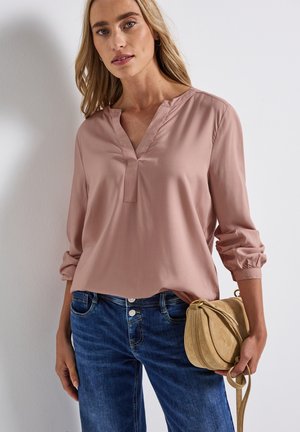 Blouse bleu clair à manches longues avec un col en V et une patte de boutonnage, associée à un jean en denim bleu et un sac bandoulière beige. Texture de tissu lisse.