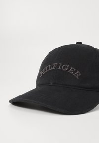 Fekete sapka textúrált anyagból, ívelt karimával és szürke hímzett "HILFIGER" logóval az elülső hónapon.