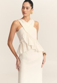 Kreemist värvi varrukatuta kleit, millel on ristumisrinnaosa ja volangiga peplum vöökoht. Sile tekstuur, minimalistlik disain ja sobiv siluett.