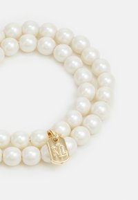 Bracciale in perle bianche con sfere tonde, texture liscia e un'etichetta dorata con il logo in rilievo 'RL'. Design semplice ed elegante adatto a varie occasioni.