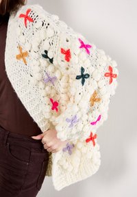 Wrap in maglia di crema chunky con accenti floreali ricamati colorati in rosso, arancio, viola e teal. Motivo testurizzato con design a punto pompom.