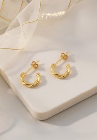 Guldvridna hoopsmycken med en polerad yta, med en baksida med stift och en rund form. Visade på en ljus marmor yta.