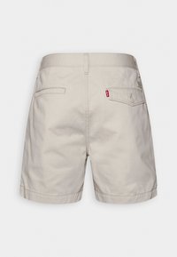 Shorts en coton beige avec un design simple, présentant deux poches arrière et un petit tag de logo Levi's rouge sur la poche droite.