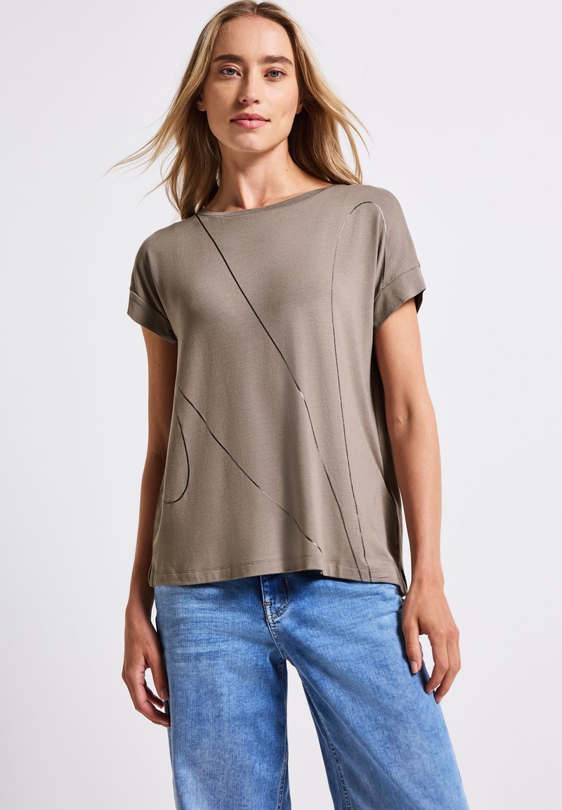 T-shirt kaki à manches courtes avec un col rond et des motifs de coutures abstraits noirs. Tissu doux et léger avec une coupe décontractée.