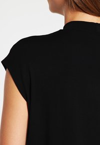 Haut noir à manches courtes avec un col arrondi, en tissu lisse et au design minimaliste, présentant la vue arrière avec de subtils détails de couture.