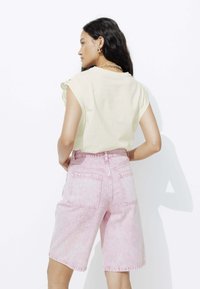 Haut court en crème à manches courtes, associé à un short en denim rose clair avec une finition délavée et deux poches arrière.