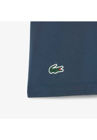 Camisa polo de color azul marino en la esquina, con un logo de cocodrilo verde bordado y un acento rojo. Textura de tela suave con un diseño de cuello típico.