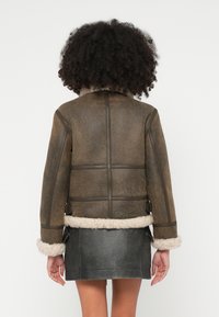 Hnedá kožená bunda s kožušinovým lemovaním, štruktúrovaným dizajnom a bočnými detailmi; doplnená tmavosivou koženou sukňou.