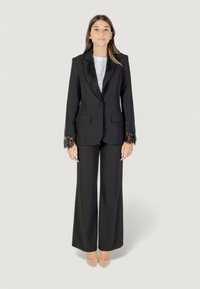 Completo nero con giacca aderente e dettagli in pizzo sulle maniche, pantaloni a gamba larga, abbinato a una maglietta bianca e tacchi nudi.